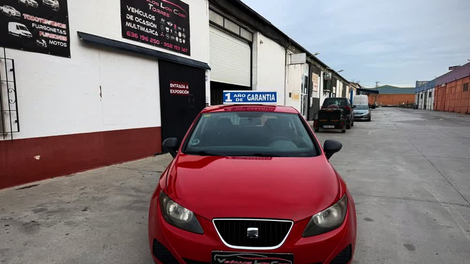 La puerta de la exposición de Low Cost Torres en la carretera de Córdoba, con un Seat Ibiza rojo de frente y el cartel azul de un año de garantía apoyado en su parabrisas